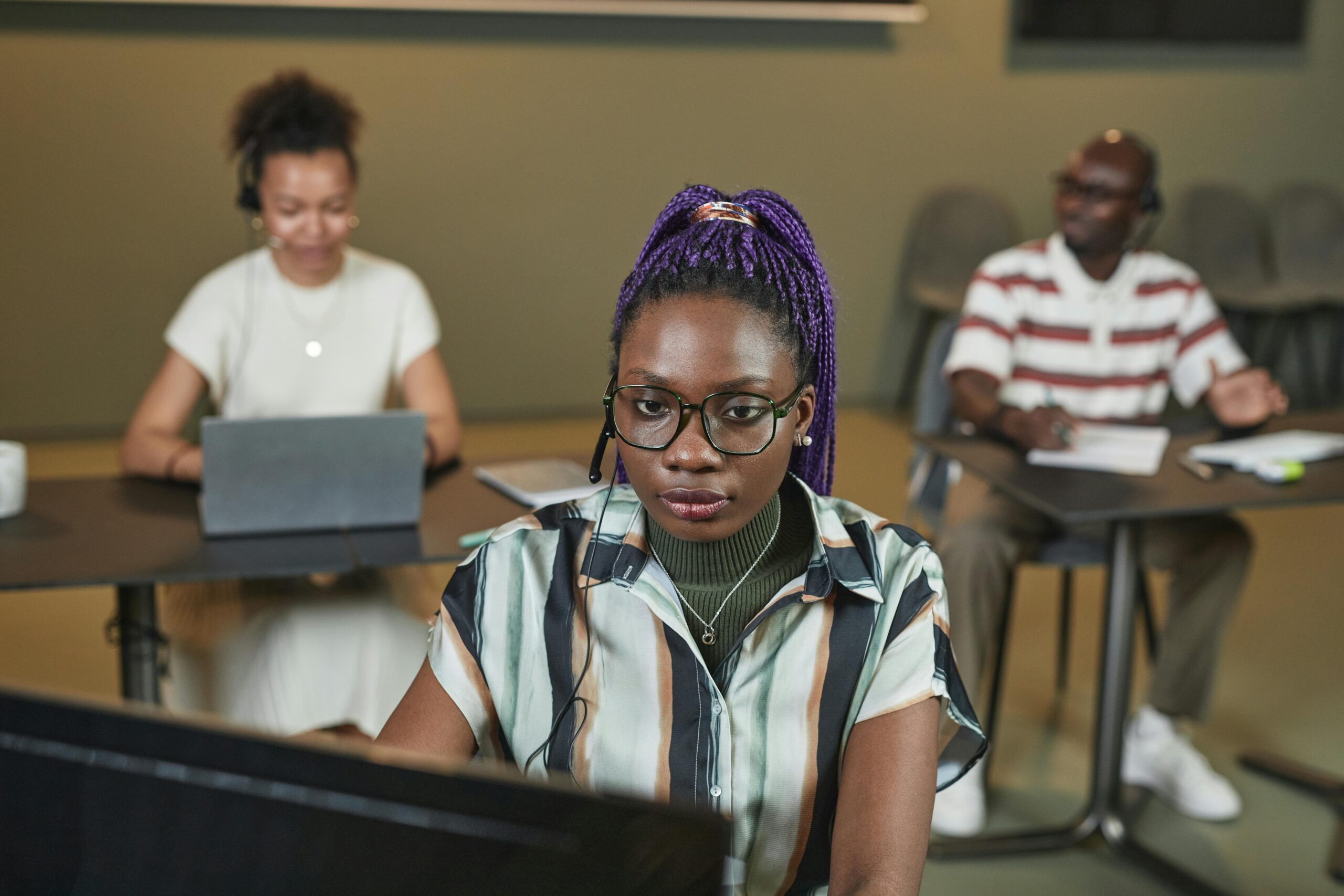 Black woman working with headset at office, colleagues in background.